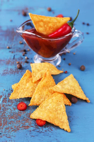 Nachos saborosos e tigela com molho na cor de fundo de madeira — Fotografia de Stock