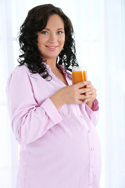 Νέα έγκυος γυναίκα που κρατά ποτήρι χυμό επάνω ελαφρύς υπόβαθρο — Φωτογραφία Αρχείου