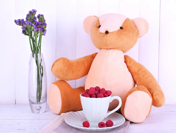 Toy bear and cup of raspberries on napkin on wooden wall background — Stock Photo, Image