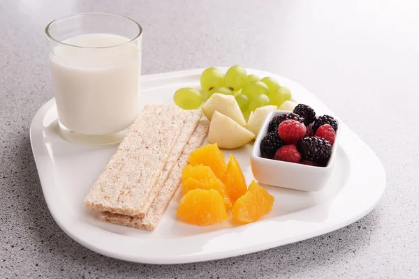Rebanadas de frutas con pan crujiente y un vaso de leche en el plato en la mesa de cerca — Foto de Stock