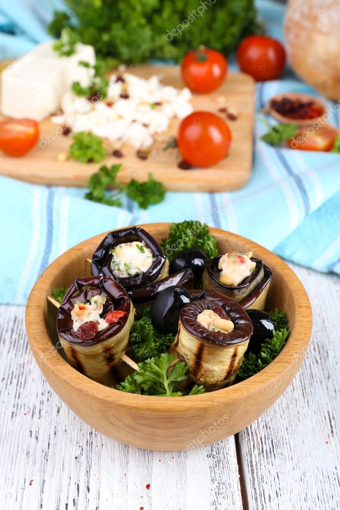 Fried aubergine in a bowl with cottage cheese, bread and parsley on a napkin on wooden background