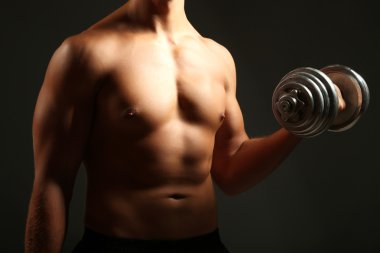 yakışıklı genç kaslı sporcu, koyu arka plan üzerinde egzersiz halter ile yürütmek