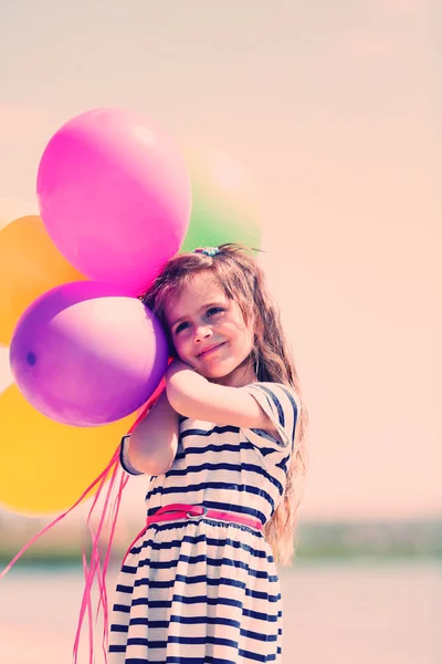 Vacker liten flicka med färgglada ballonger på stranden — Stockfoto
