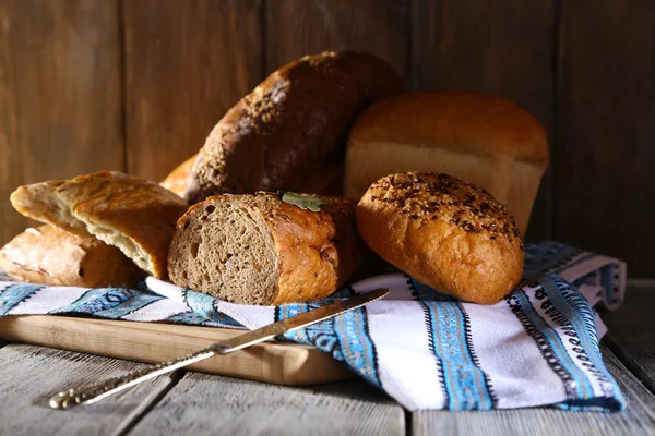 Composição de pão fresco assado, faca e toalha de cozinha, sobre fundo de madeira — Fotografia de Stock