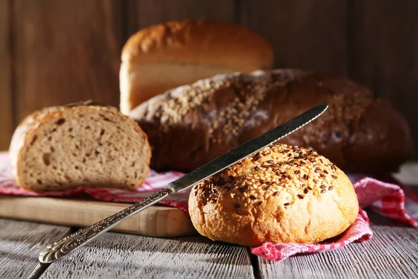 Samenstelling van vers gebakken brood, mes en keuken handdoek, op houten achtergrond — Stockfoto