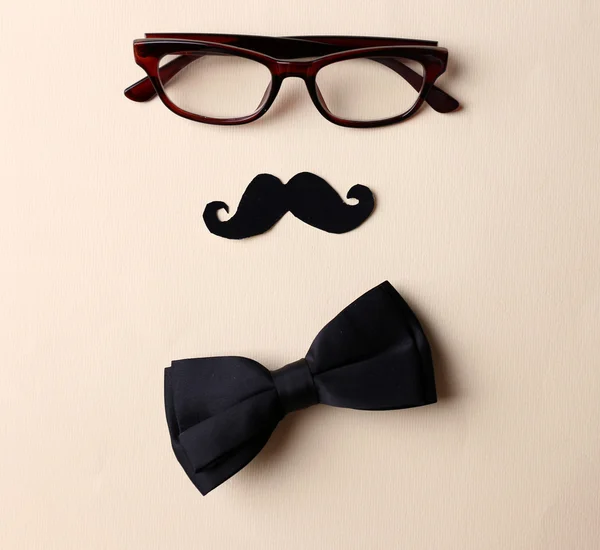 Glasses, mustache and bow tie forming man face on beige background — Stock Photo, Image