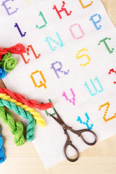 Handgefertigte bestickte Buchstaben auf weißem Stoff und Schere auf hölzernem Hintergrund — Stockfoto