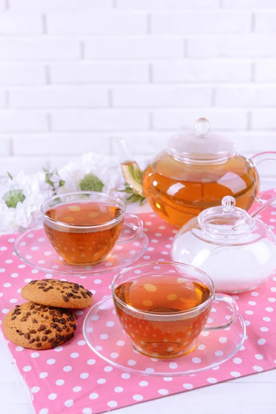 Theepot en kopjes thee op tafel op bakstenen muur achtergrond — Stockfoto