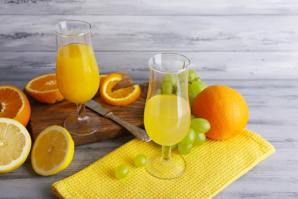 Glasses of juice with fresh fruits on grey wooden table — Stock Photo, Image