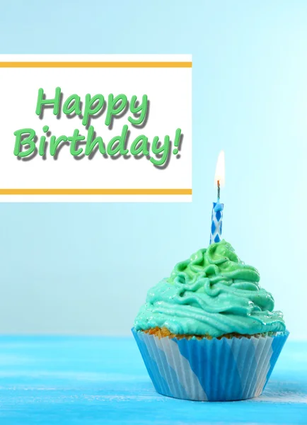 Delicious birthday cupcake on table on light blue background