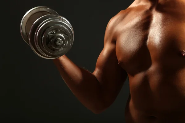 Bonito jovem desportista muscular executar exercício com halteres no fundo escuro — Fotografia de Stock