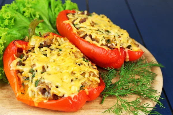 Stuffed red peppers with greens on wooden stand on table close up — Stock Photo, Image