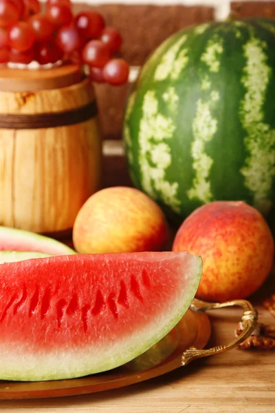Composition of ripe watermelon, fruits and wooden barrel on  color wooden table, on bricks background — Stock Photo, Image