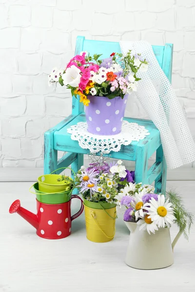 Strauß bunter Blumen in dekorativen Eimern, auf Stuhl, auf dem heimischen Innenhintergrund — Stockfoto