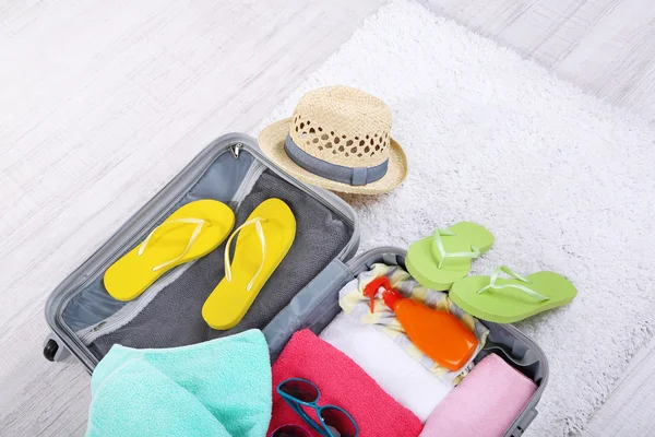 Koffer met dingen op witte tapijt op de vloer voor reizen ergens dicht bij water voor de besteding van de zomervakantie — Stockfoto