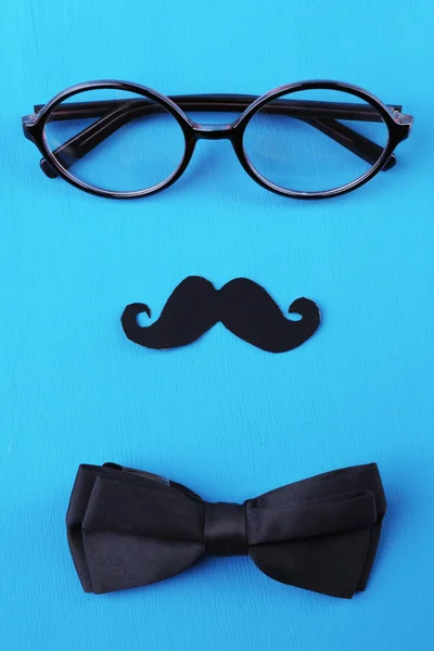 Glasses, mustache and bow tie forming man face on color background — Stock Photo, Image