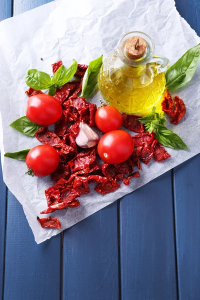 Tomates séchées au soleil dans un bocal en verre, huile d'olive en bouteille en verre, feuilles de basilic sur fond en bois de couleur — Photo