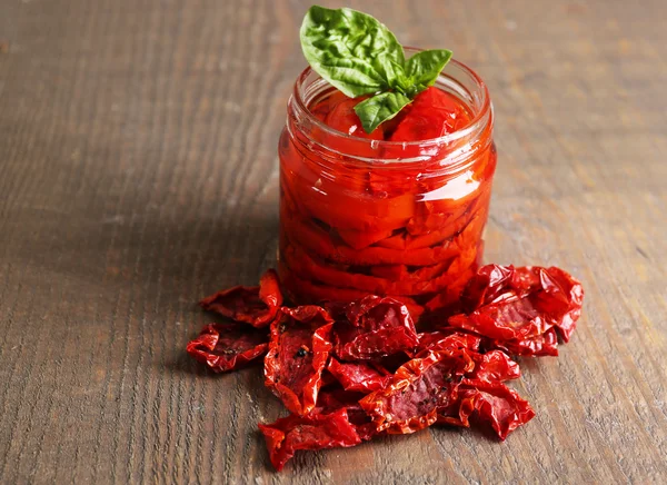 Tomates séchées au soleil dans un bocal en verre, feuilles de basilic sur fond en bois — Photo