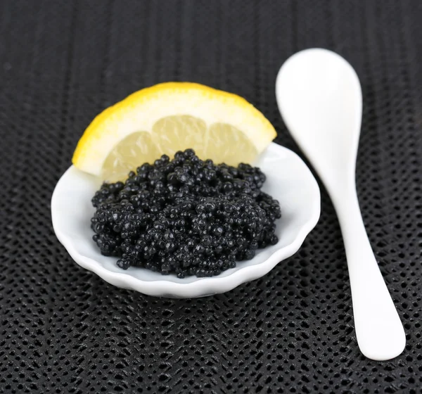 Caviale nero con limone su piatto su sfondo tessuto scuro — Foto Stock