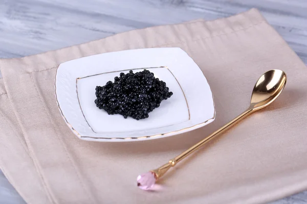 Caviar negro en plato sobre servilleta sobre fondo de madera — Foto de Stock