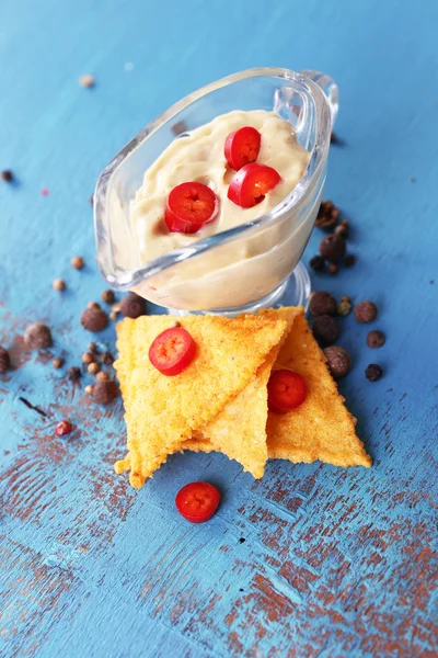 Nachos saborosos e tigela com molho na cor de fundo de madeira — Fotografia de Stock