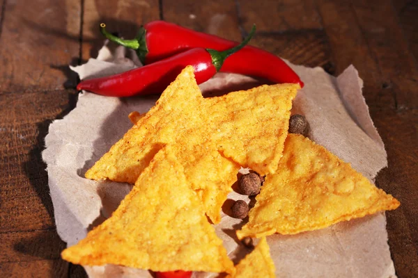 Tasty nachos and chili pepper on paper, on wooden background — Stock Photo, Image