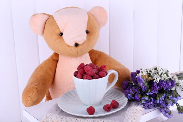 Oso de juguete y taza de frambuesas sobre fondo de pared de madera — Foto de Stock