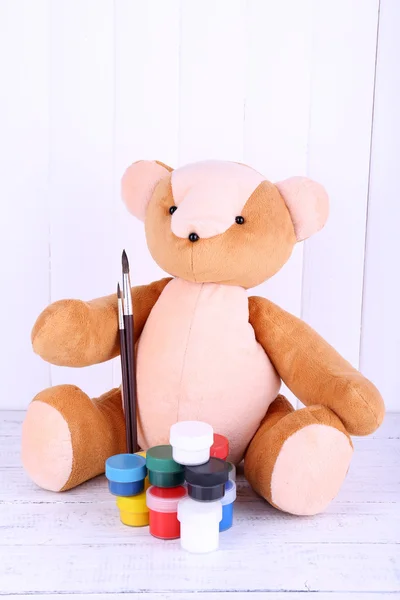 Toy bear and paints on wooden wall background — Stock Photo, Image