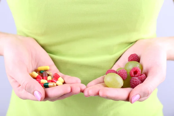 灰色の背景に果実や薬を保持している女性 — ストック写真