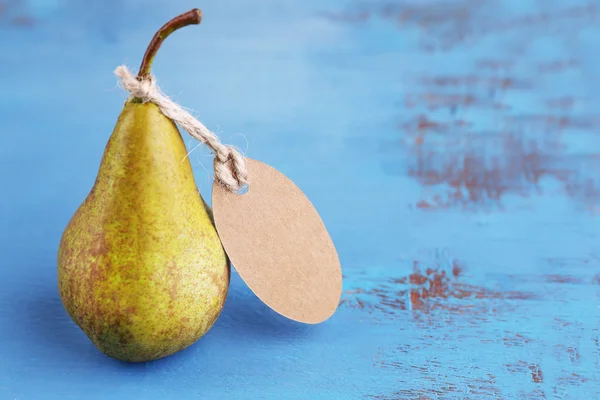 Ripe pear with paper tag on wooden background — Stock Photo, Image
