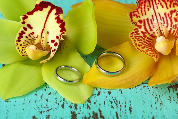 Obrączki ślubne i kwiaty orchidei, szczegół, na tle drewniane kolor — Zdjęcie stockowe