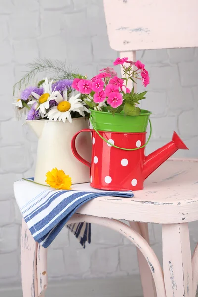 Bouquet of colorful flowers in decorative buckets, on chair, on light wall background — Stock Photo, Image