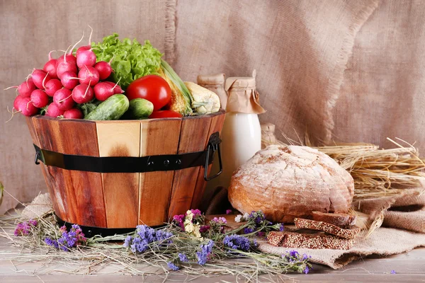 Big round wooden basket with vegetables, milk and bread on sacking background — Stock Photo, Image