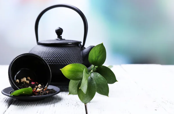 Tetera negra, tazón y té en la mesa de madera de color, sobre fondo brillante —  Fotos de Stock