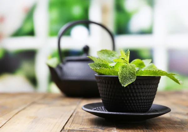 Teko Cina tradisional dengan daun mint segar di atas meja kayu, dengan latar belakang cerah — Stok Foto