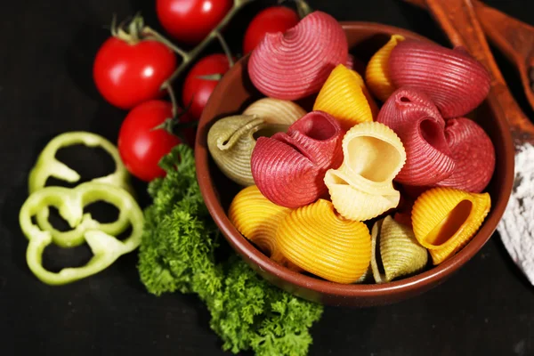 Composition de pâtes colorées dans un bol, tomates fraîches, persil sur fond bois foncé — Photo