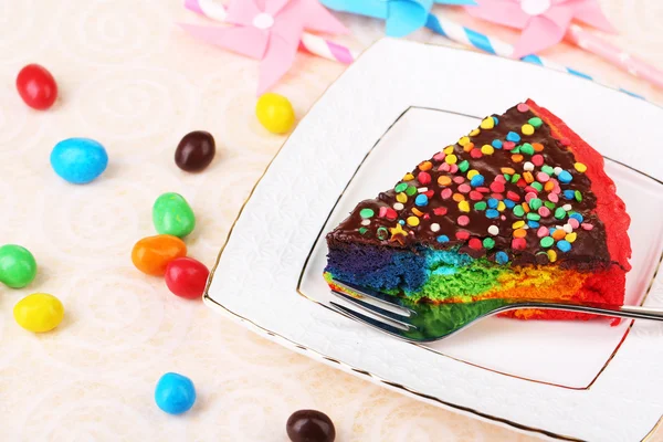 Delicious rainbow cake on plate, on tablecloth background — Stock Photo, Image