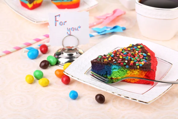 Deliziosa torta arcobaleno su piatto e tazza con caffè, sul tavolo, su sfondo chiaro — Foto Stock