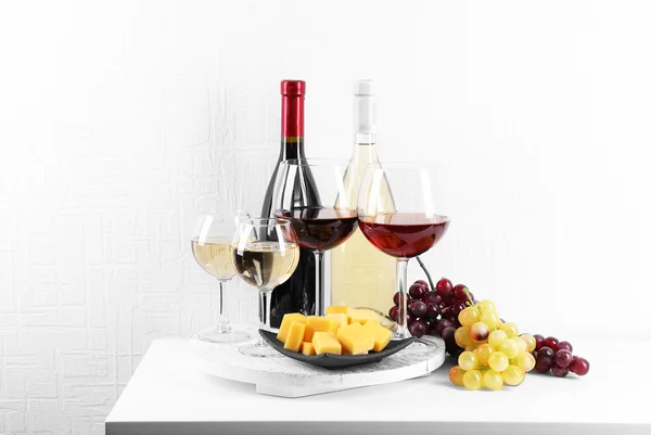 Bouteilles et verres de vin, fromage et raisins mûrs sur la table dans la chambre — Photo