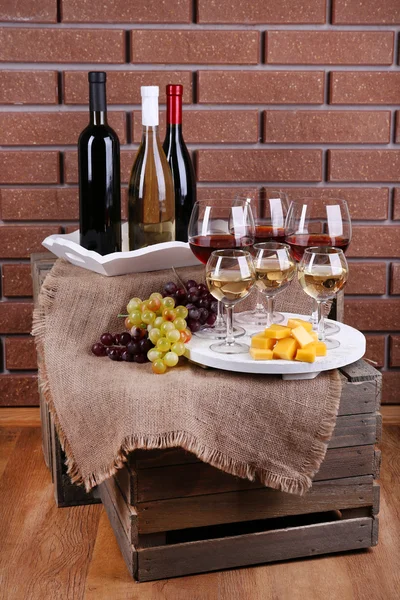 Botellas y vasos de vino, queso y uvas maduras en la mesa sobre fondo de pared de ladrillo —  Fotos de Stock