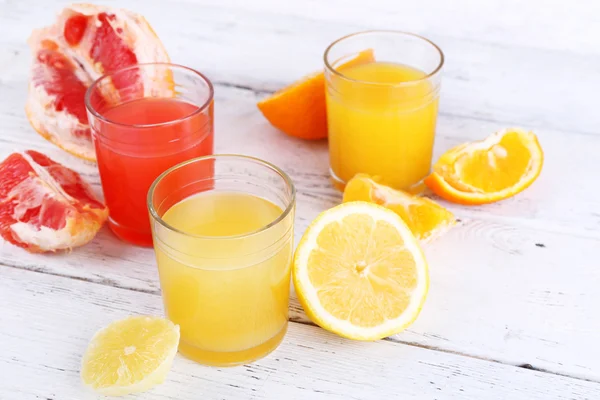 Different sliced citrus fruits and glasses of juice on wooden table — Stock Photo, Image