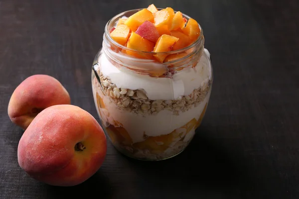 Desayuno saludable yogur con melocotón fresco y muesli servido en frasco de vidrio, sobre fondo de madera — Foto de Stock