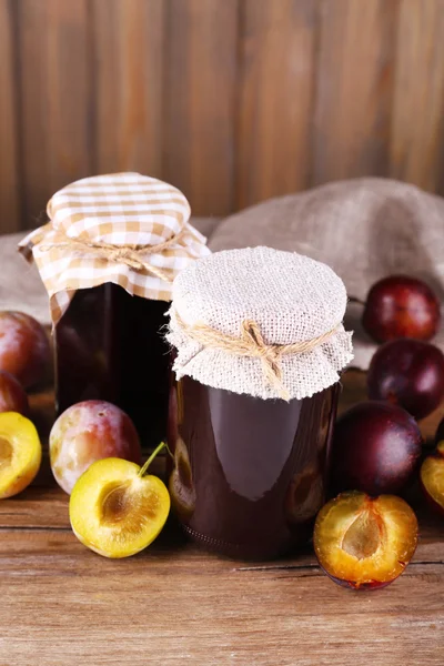 Confiture de prunes savoureuse dans des bocaux et des prunes sur table en bois sur fond en bois — Photo