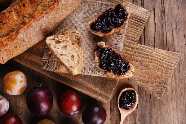 Brød med plommesyltetøy og plommer på trebord. – stockfoto