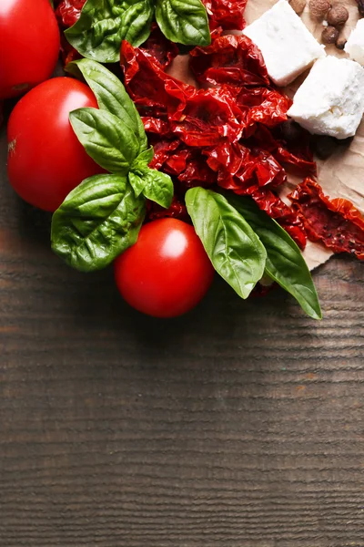 Sušenými a čerstvá rajčata, bazalkové listy a feta sýr na barevné dřevěné pozadí — Stock fotografie