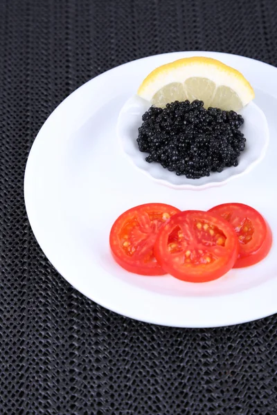 Caviar negro con rodajas de tomate en plato sobre fondo de tela oscura —  Fotos de Stock