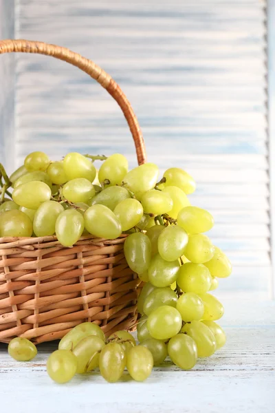 Ripe grapes in wicker basket on wooden table on light background