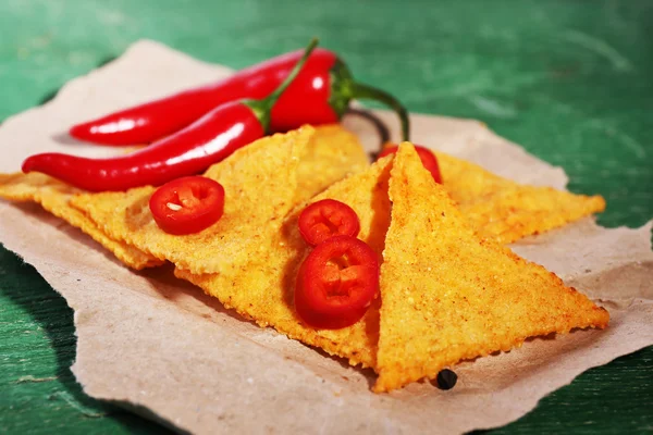 Smaczne nachos i papryka chili na papierze, na tle drewniane — Zdjęcie stockowe