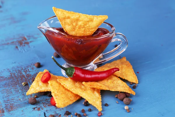 Nachos saborosos e tigela com molho na cor de fundo de madeira — Fotografia de Stock