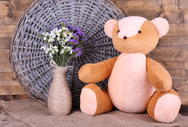Игрушечный медведь и ваза полевых цветов на мешковине на фоне деревянной стены — стоковое фото